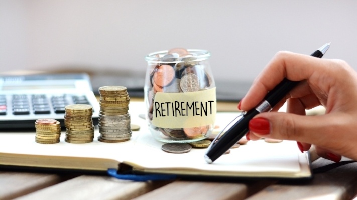 Concept of retirement planning with woman putting coins in glass jar for pension
